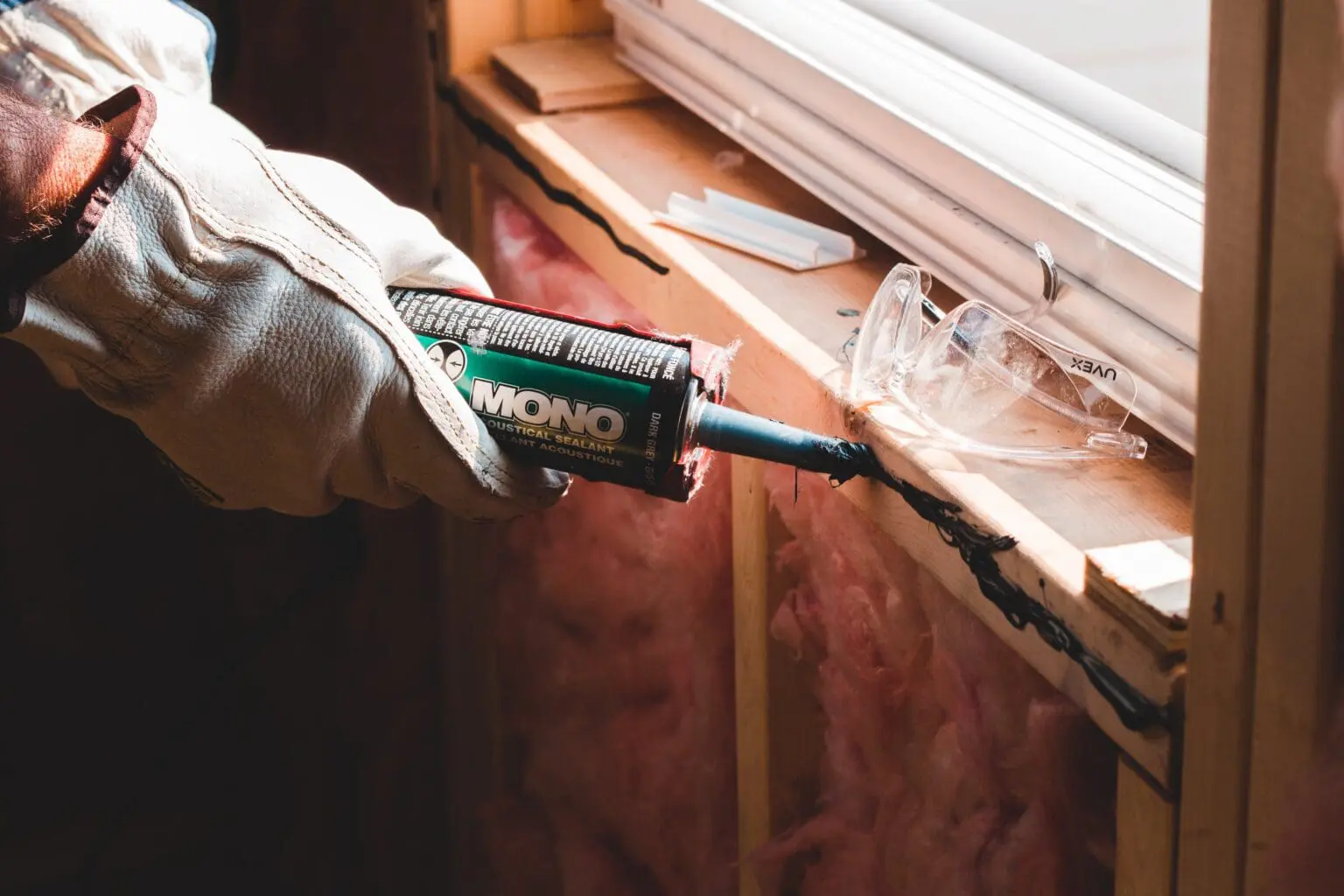 Contractor Using a Glue Gun to Seal Air Leakage Next to a Window A contractor is using a glue gun next to a window to seal up air leakage, improving the home's energy efficiency
