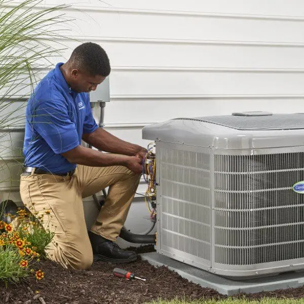 An AC repair technician is working on an air conditioner outside at a rental property, performing necessary repairs to ensure the system functions properly