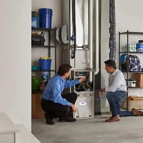 Two people working on a furnace in a garage.