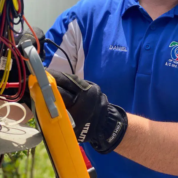 AC Technician Holding an Electrical Wire and Meter for System Testing An AC technician is holding an electrical wire and a meter, testing the electrical components of an air conditioning system to ensure proper functionality