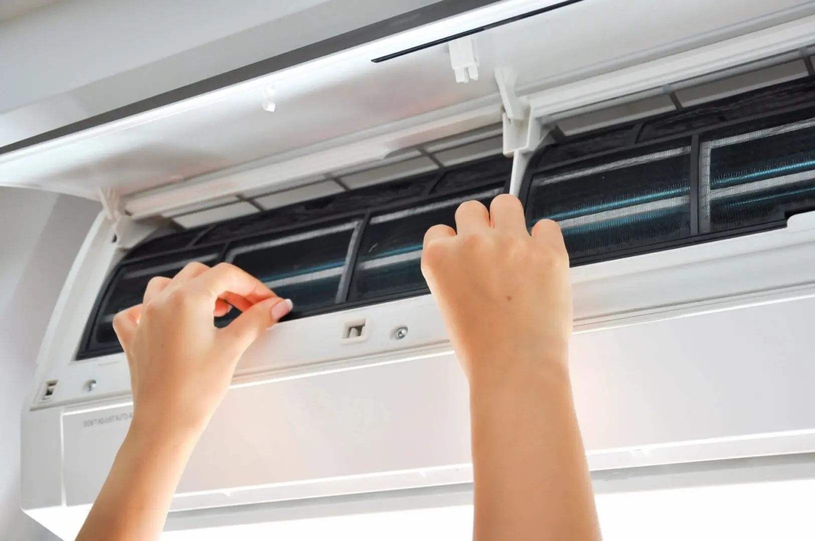 An air conditioning repair technician is working on an air conditioner inside, likely performing maintenance or repairs