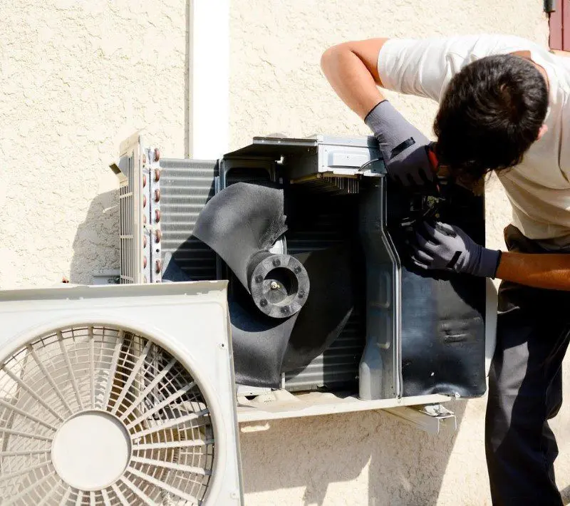 A HVAC Technician repairing an air conditioner outside.