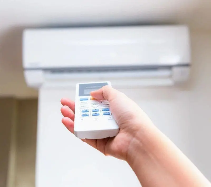 A person is holding a remote control in their hand to control a residential ac unit