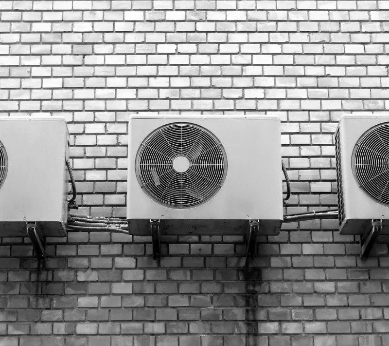 Three air conditioners mounted to the side of a brick wall.