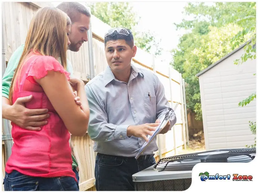 Air Conditioning Service Man and Homeowners Reviewing New Heat Pump Installation An air conditioning service man and the homeowners are going over the details of the newly installed heat pump, discussing its operation and benefits