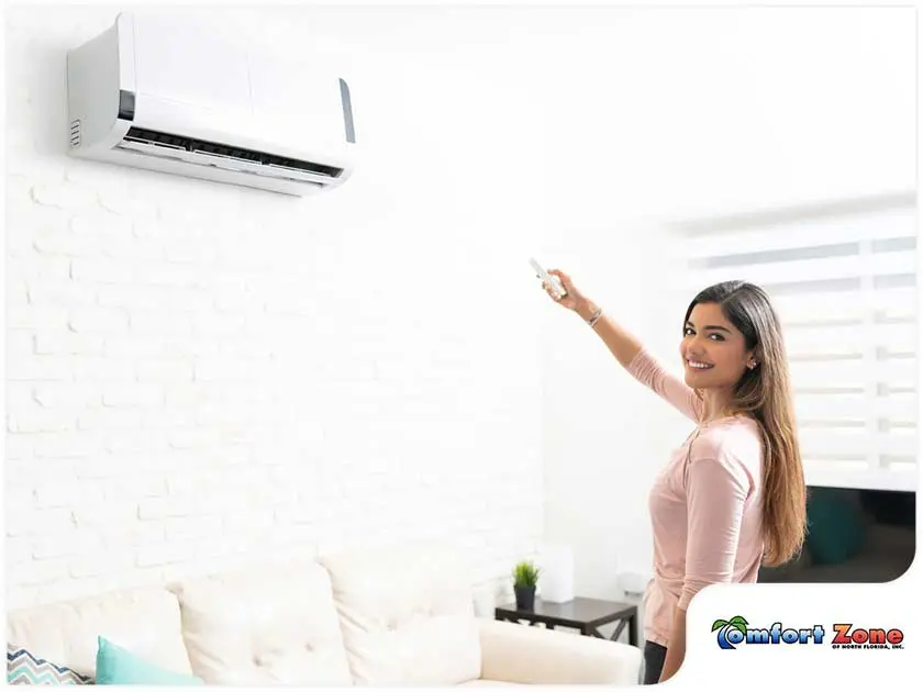 Woman Smiling in Front of New Ductless Cooling Unit Installation A woman is standing in front of a ductless cooling unit, smiling and happy about her new installation, enjoying the comfort of her upgraded system