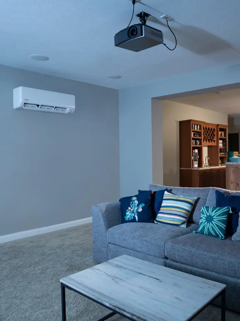 A living room features a comfortable couch with a ductless air conditioning unit mounted on the wall above, providing efficient cooling for the space