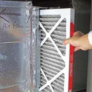 A person is inspecting and touching the air filter of an air conditioner, preparing to clean or replace it for optimal system performance