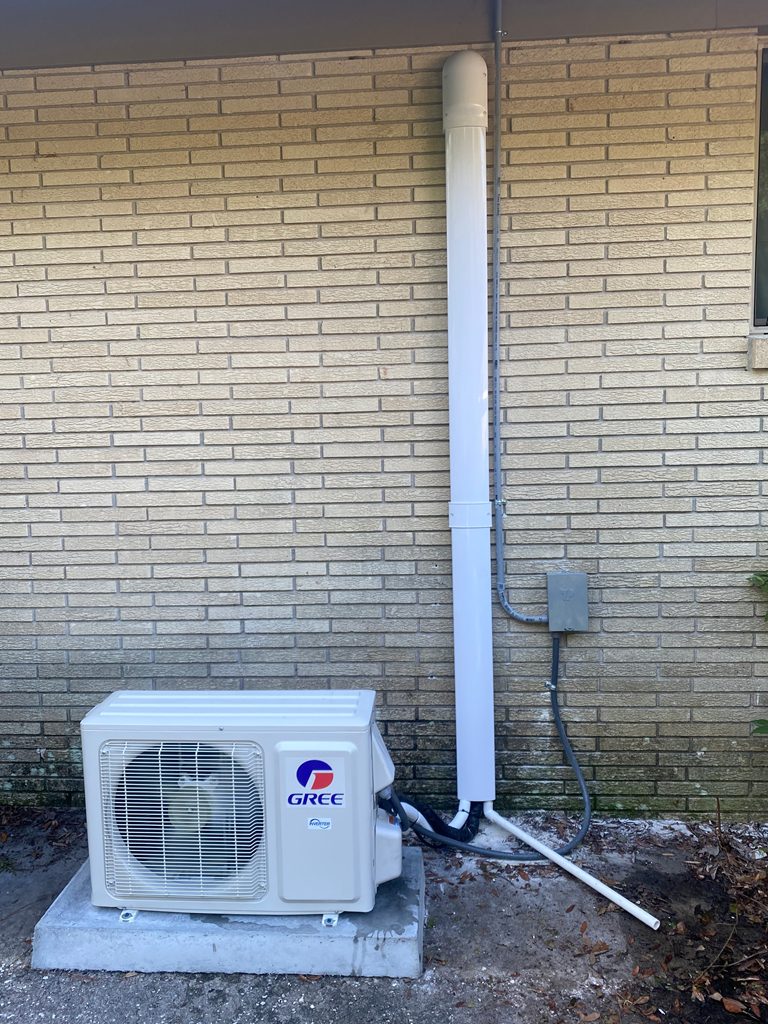 A white air conditioner is installed outside a building, mounted on a concrete surface, ready to provide cooling for the interior.