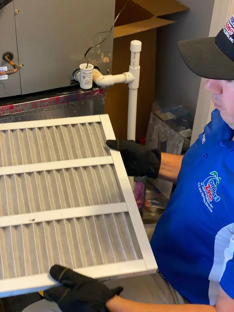 A man is holding an air filter in his hand, inspecting and preparing to replace it in an HVAC system