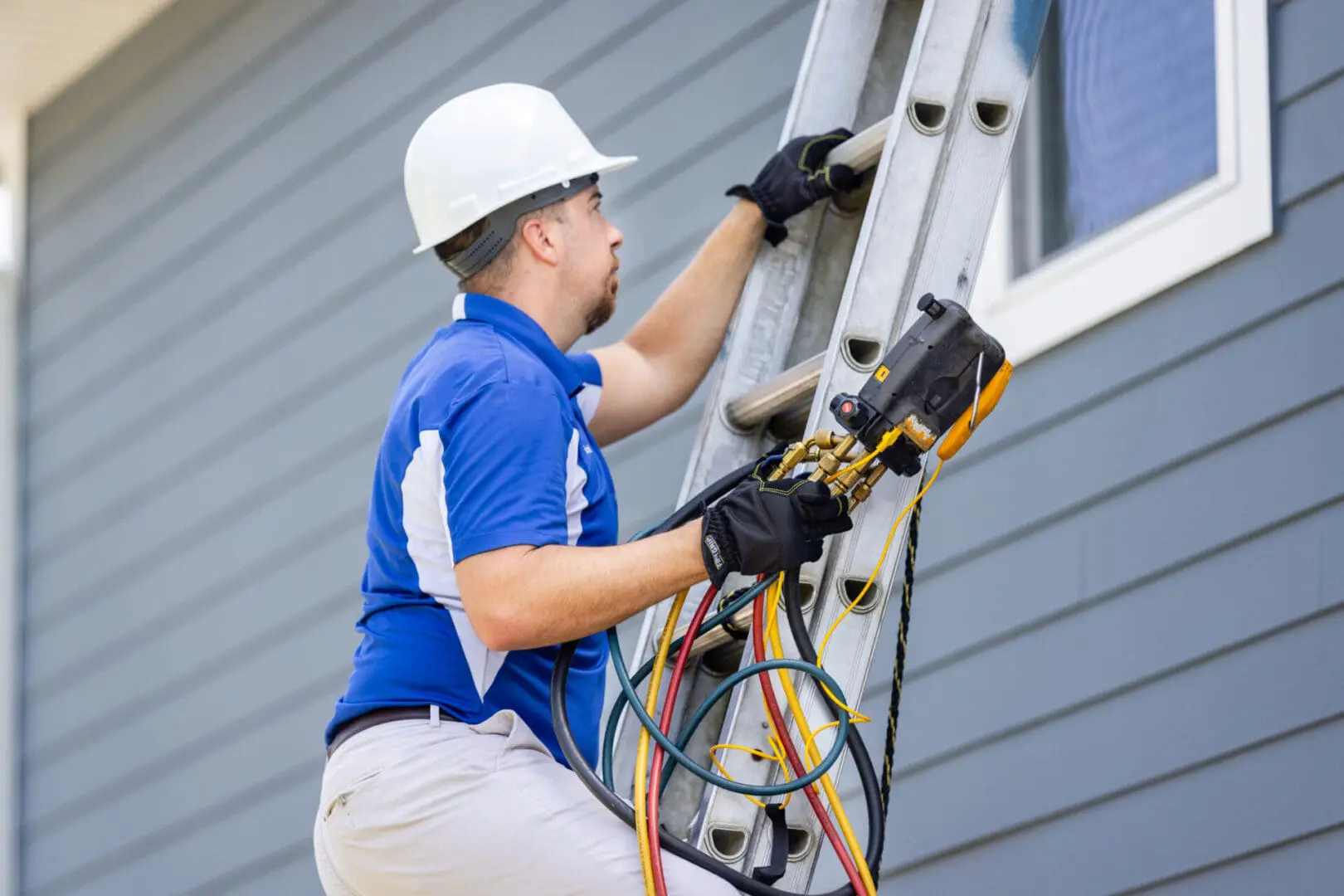 A commercial HVAC service technician is climbing a ladder to reach and service an air conditioning unit mounted on the roof of a building, preparing for maintenance or repairs.