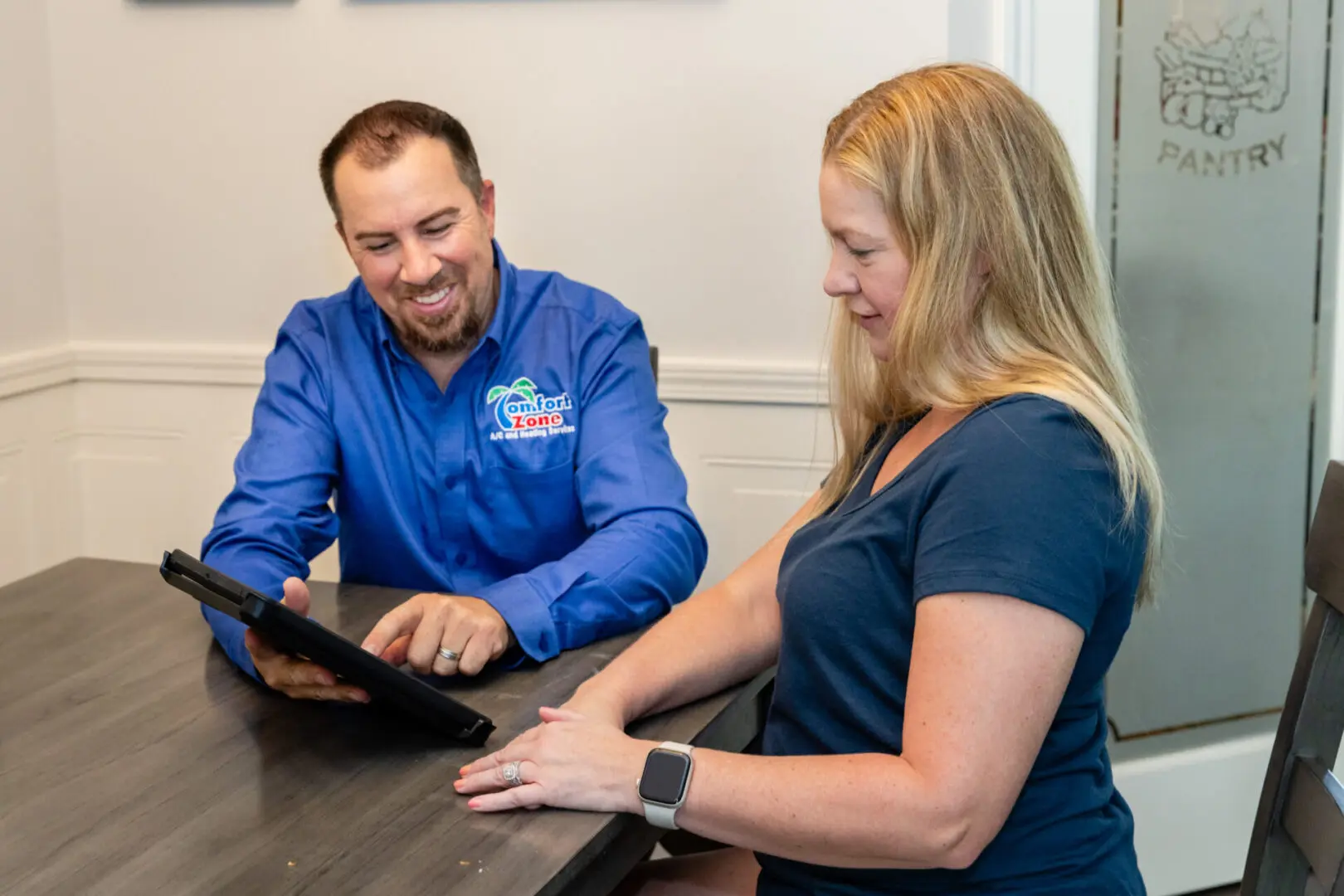 A HVAC consultant and homeowner sitting at a table with an iPad reviewing a replacement proposal.