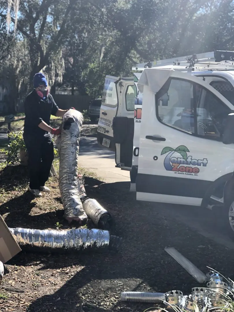 AC Technician removing flexible duct wearing a pink mask with gloves in front of a company van