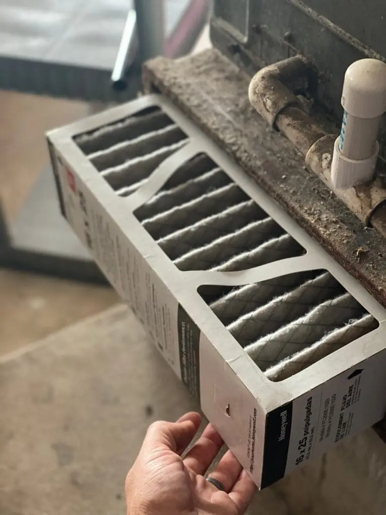 Dirty air conditioning filter during maintenance, reducing airflow and system efficiency in an AC unit.