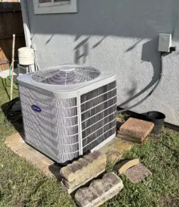 Carrier air conditioning condenser on a concrete pad by a residential home with bricks around the unit.