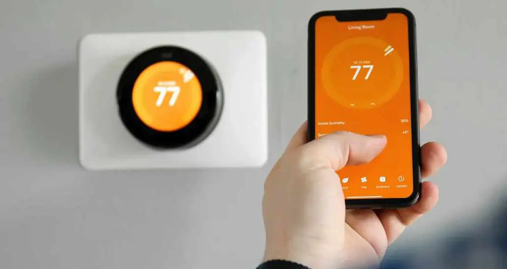 smart thermostat Hand holding phone controlling smart thermostat at 77°F