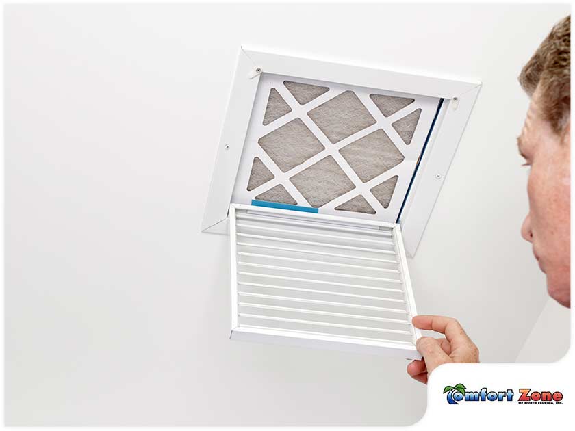 A person inspecting an air conditioning filter in a ceiling vent to check its cleanliness.