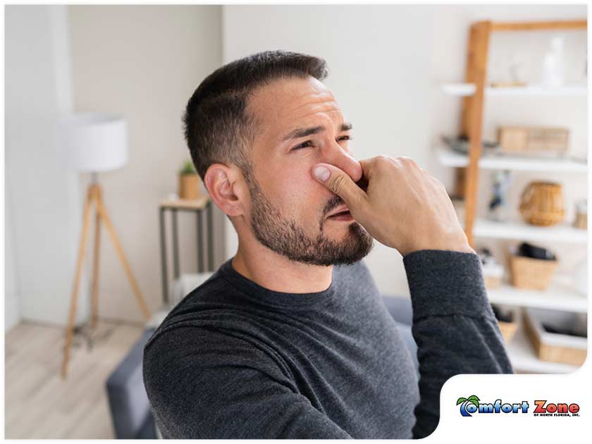 A man is holding his nose while looking at the camera, indicating discomfort due to poor indoor air quality in the home