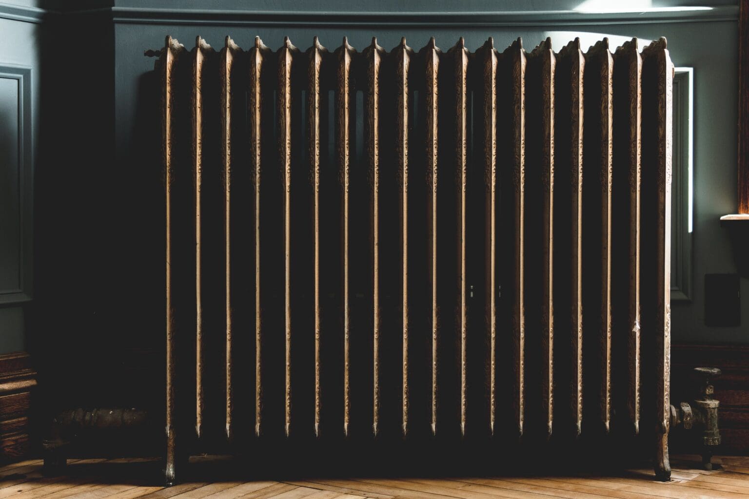 Vintage radiator against a dark wall in a dimly lit room, showcasing a classical design with prominent vertical ribs.