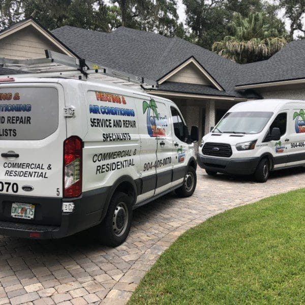 Two branded hvac service and repair vans parked in a residential driveway, with trees and a house in the background.