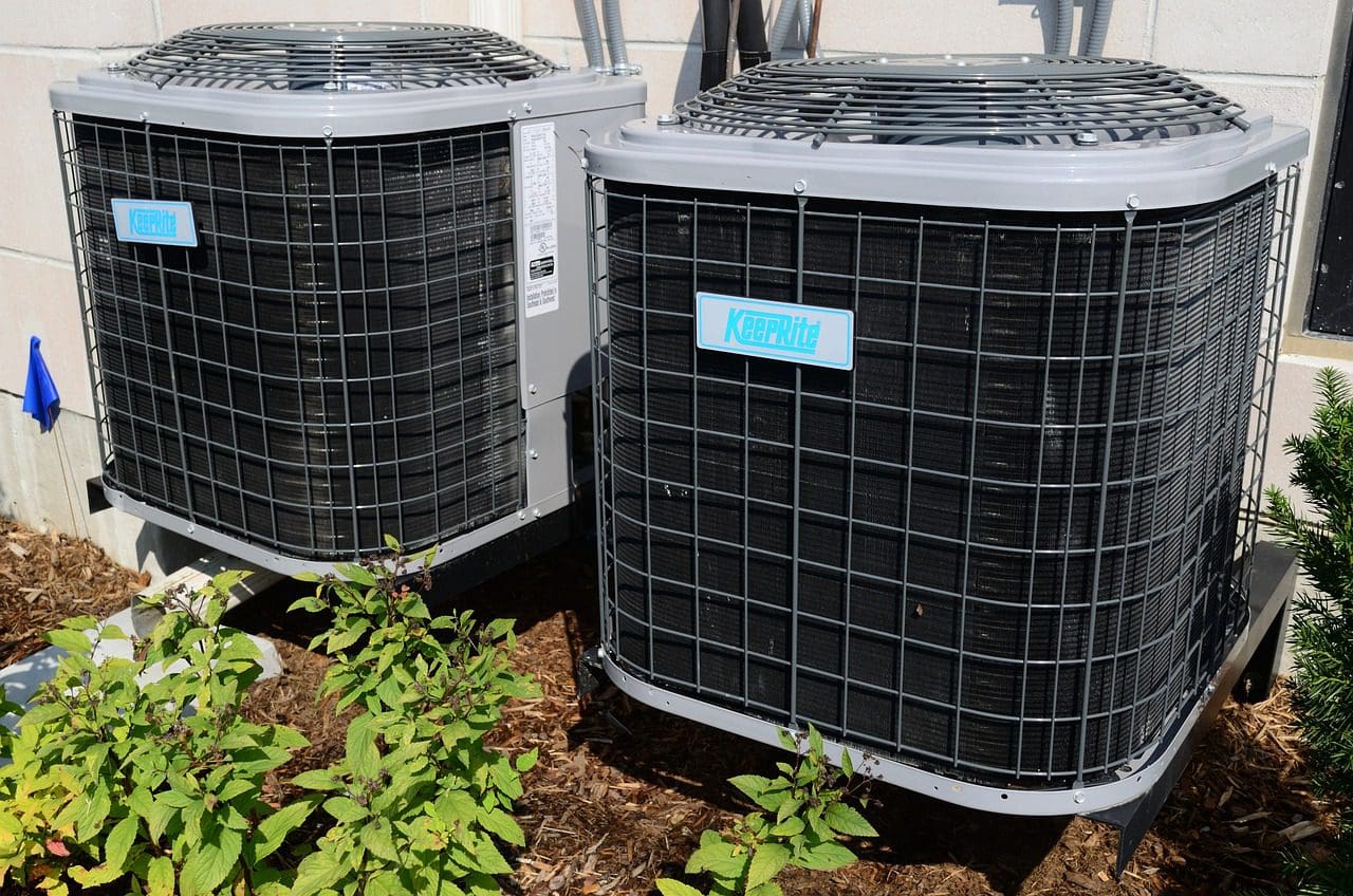 Two outdoor air conditioning units beside a building, with surrounding shrubbery. each unit features a visible brand label.