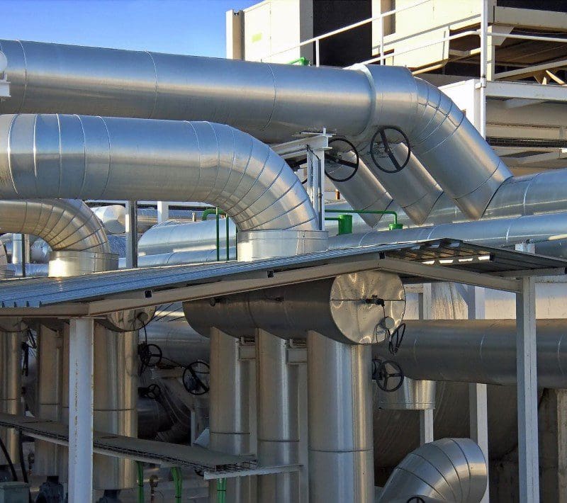 A large metal pipe system in front of some buildings.