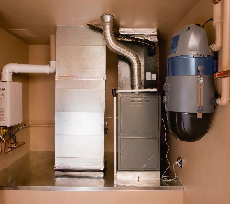 A home utility room with a furnace, water heater, and central vacuum system installed along a beige wall.