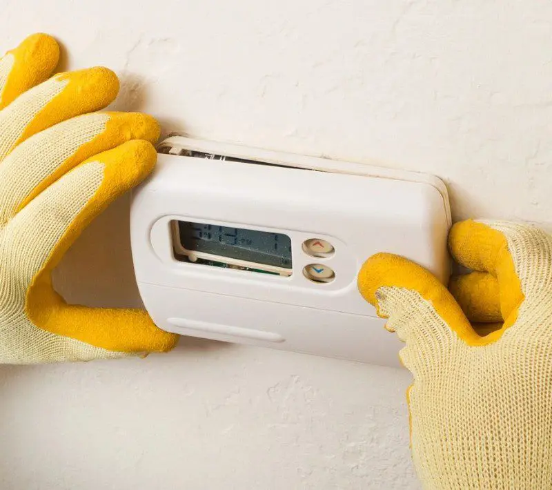 A gloved hand installing a thermostat.