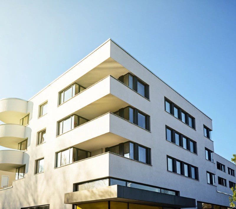Modern white apartment building with balconies and clear blue sky in the background.