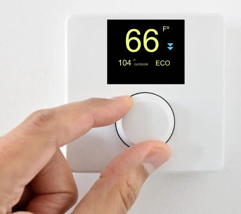 A hand adjusting a thermostat on a wall.