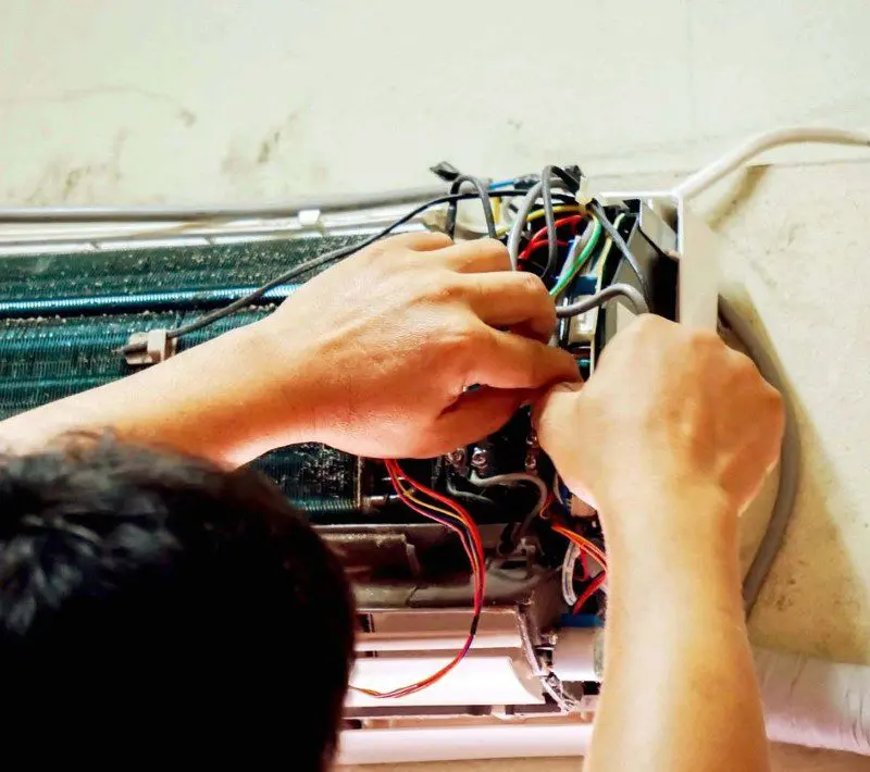 A person working on wires in front of an air conditioner.