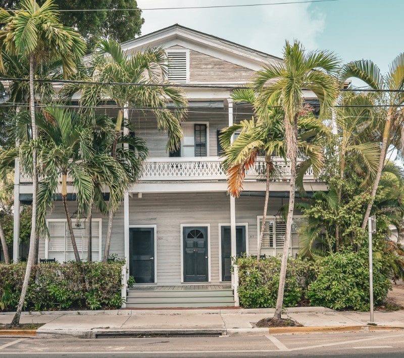 A two-story house with a porch and palm trees in front.