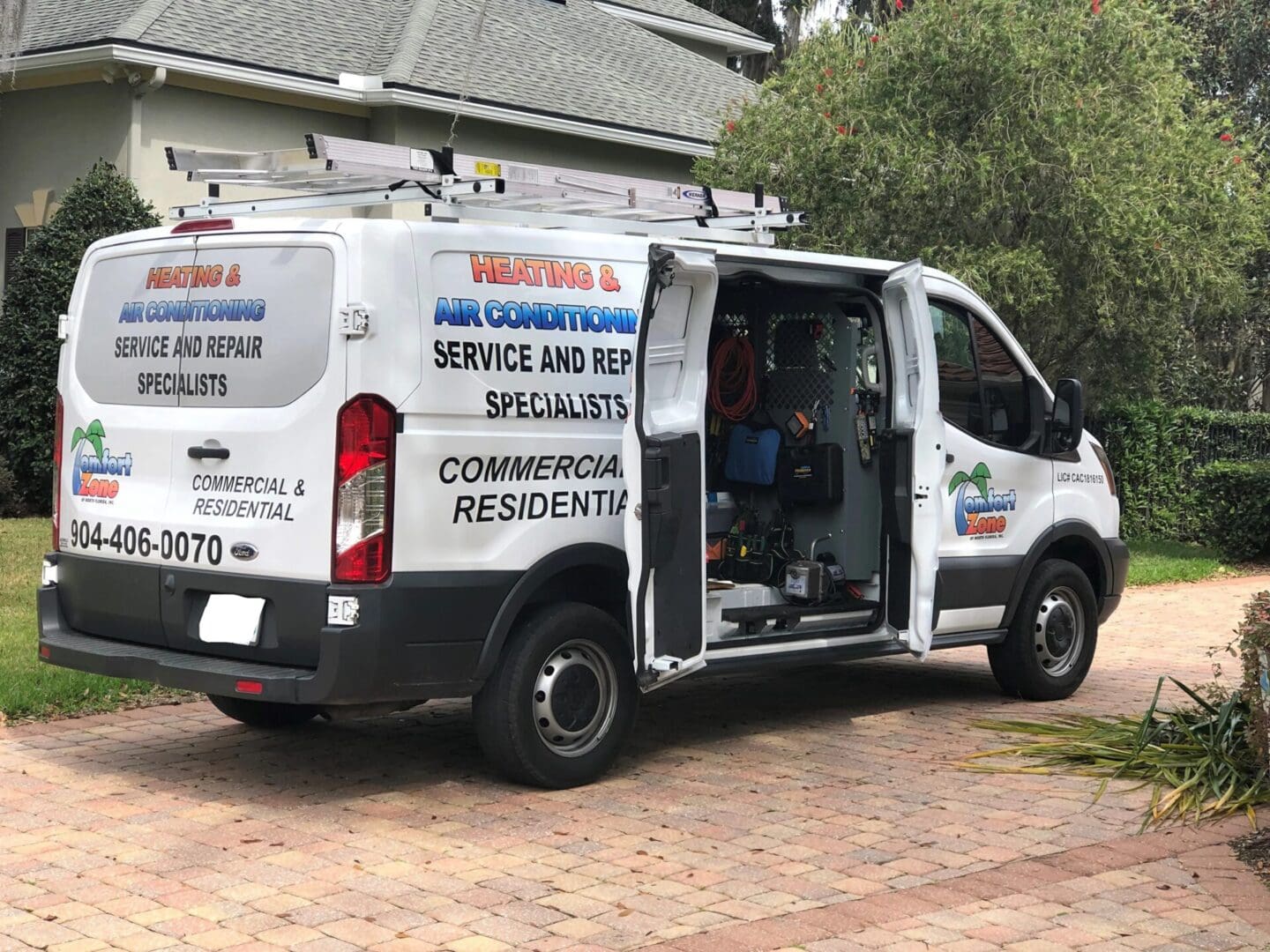 A white hvac service van with open back doors, revealing tools and equipment, parked in a residential driveway.