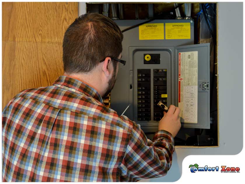 A man in a plaid shirt examines an open electrical panel, adjusting switches inside, with a "comfort zone" logo in the corner.