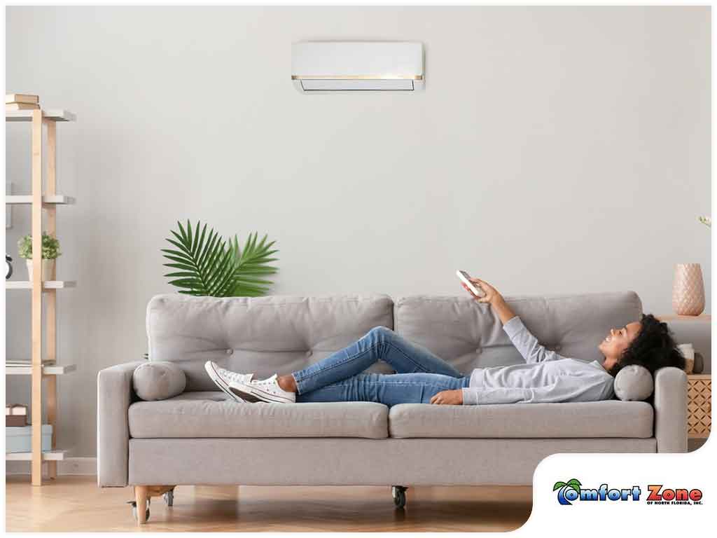A woman relaxing on a sofa while using a remote control under an air conditioning unit in a modern living room.
