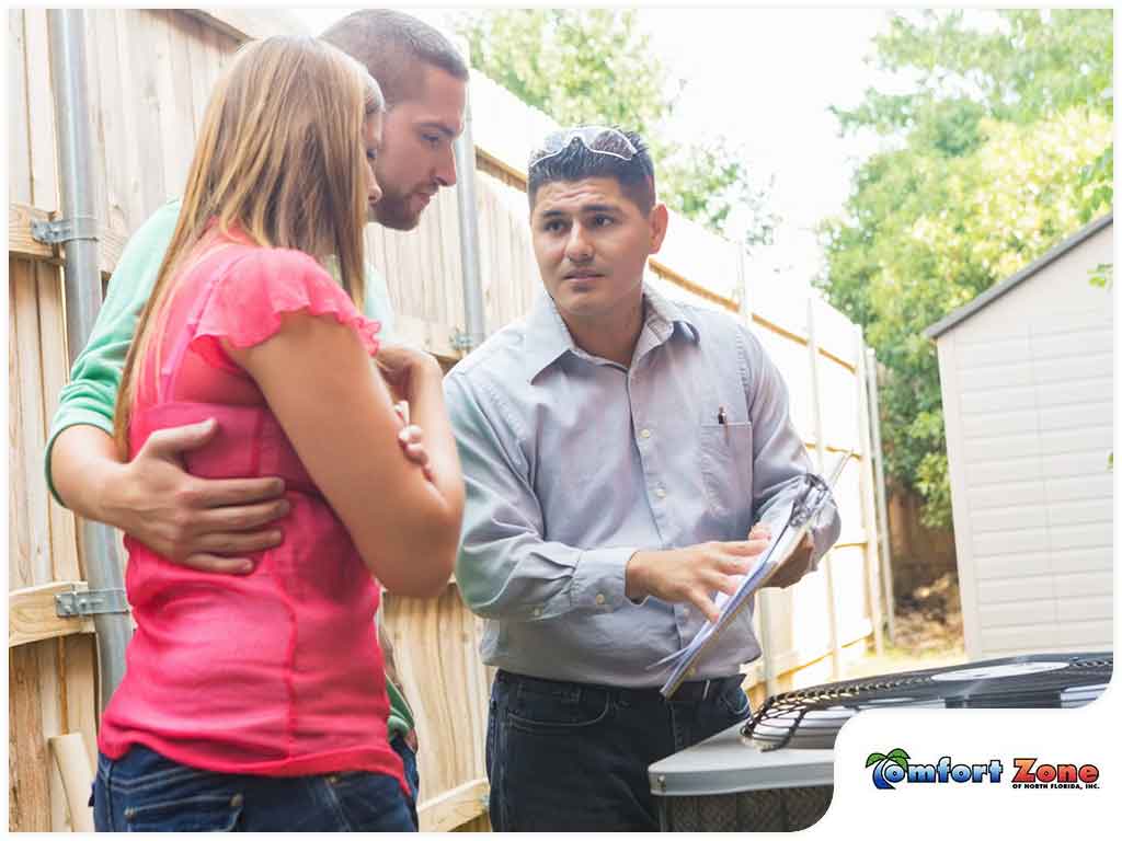A technician discusses hvac maintenance with a couple next to their home, holding a clipboard.