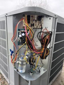Inside the electrical panel of an air conditioning unit with a defrost control board, capacitor and contactor.