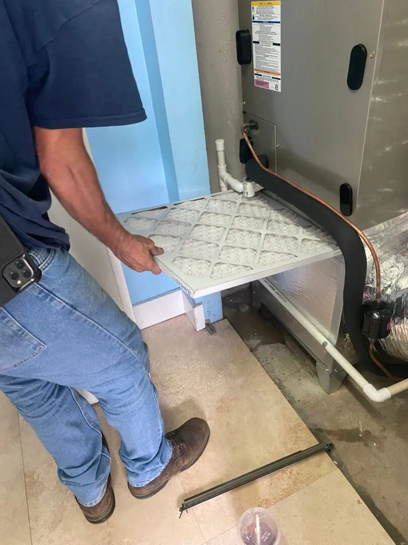 Technician replacing the air filter in an hvac system, showing a partial view of the person and the unit in a utility room.