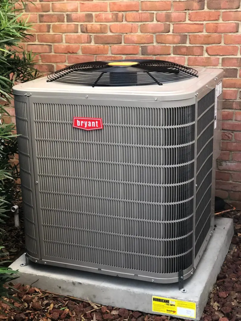 Outdoor bryant air conditioning unit installed on a concrete pad next to a brick wall, with visible safety labels.