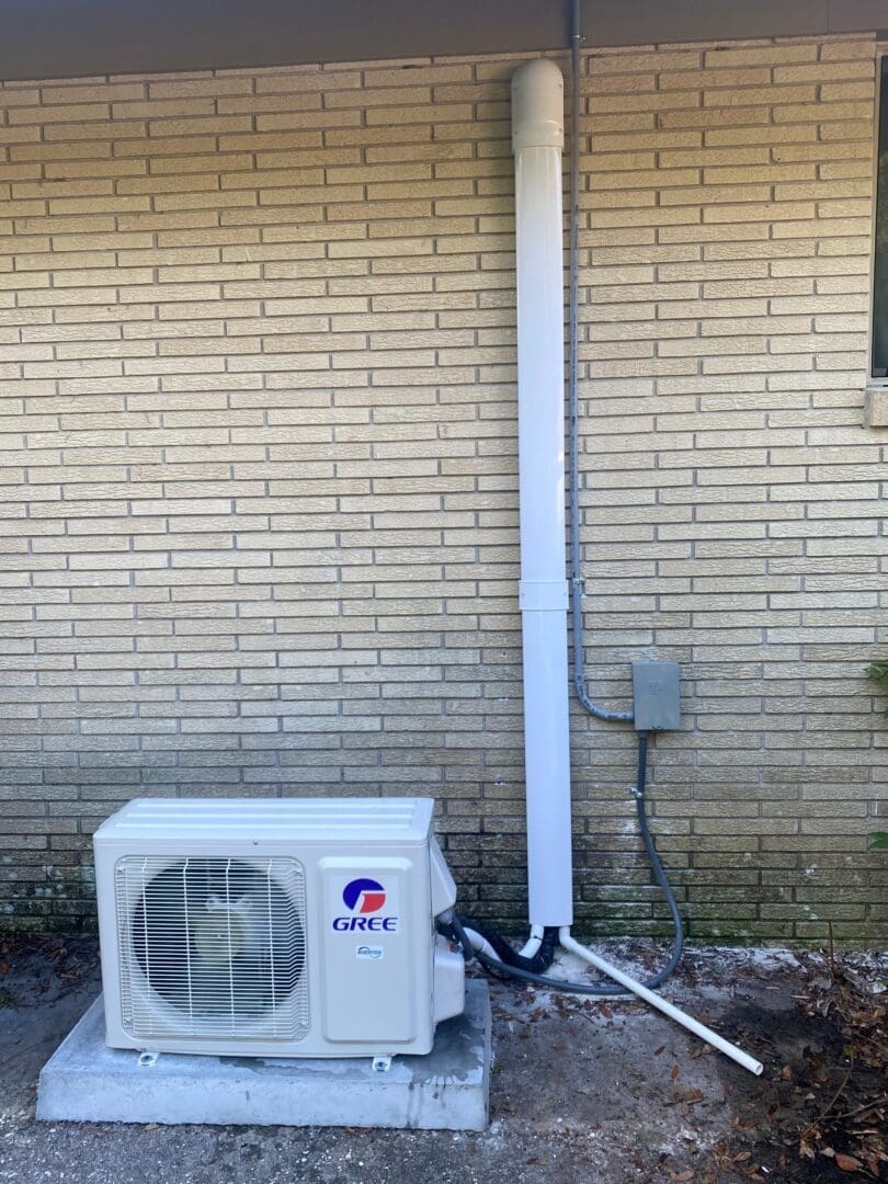 An outdoor hvac unit next to a beige brick wall with a large white vertical drainpipe and electrical conduit.