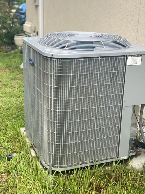 A residential outdoor air conditioning unit standing on a grassy area beside a building.