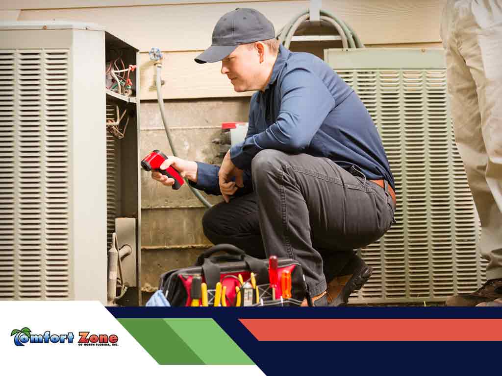 A technician repairs a large air conditioning unit, equipped with tools and a flashlight, focusing intently on his work.