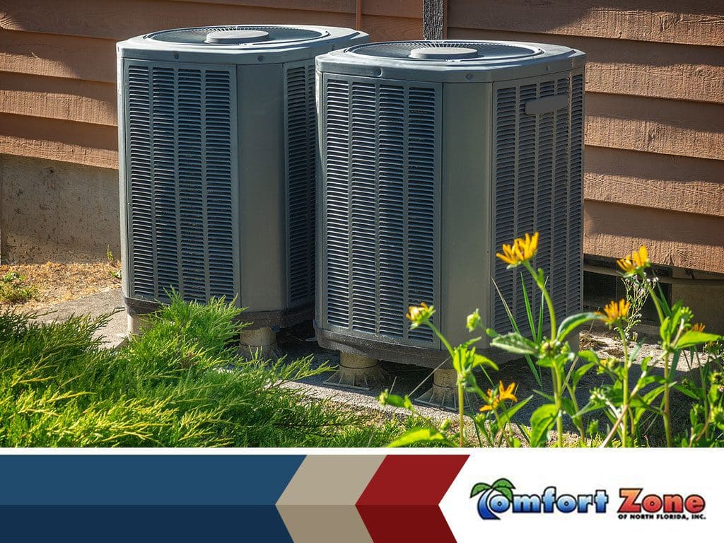 Two gray air conditioning units beside a house with yellow flowers in the foreground.