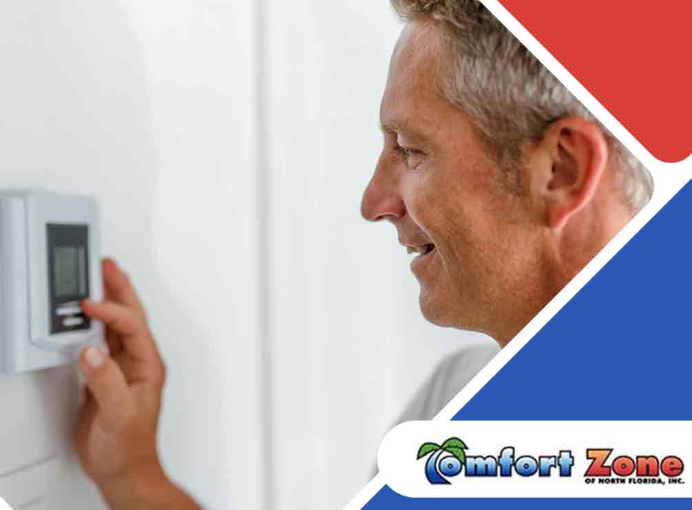 Middle-aged man adjusting a digital thermostat on a wall, smiling, with a business logo in the corner.