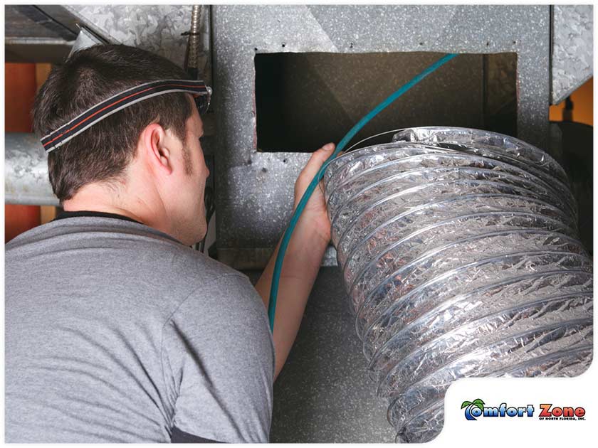 A technician installs flexible ductwork into an hvac system in a ceiling, wearing a headlamp for visibility.