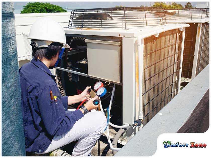 A technician wearing a helmet uses gauges to check an outdoor hvac unit on a sunny day.