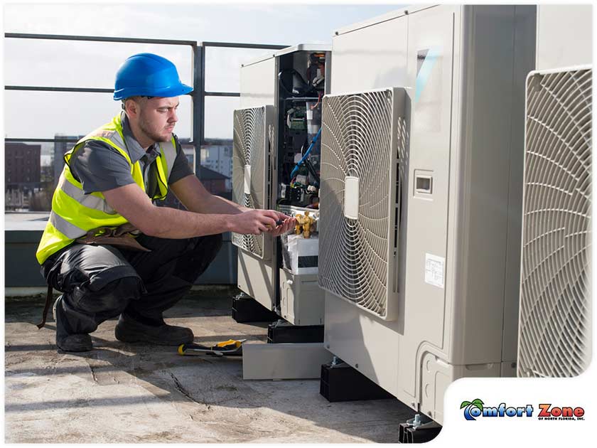 A man in yellow vest and hard hat fixing an air conditioner.