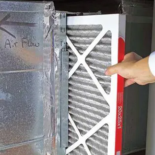 Person installing a new air filter into an hvac system, showing the airflow direction.