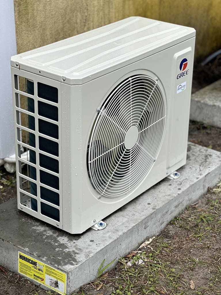 Outdoor hvac unit by gree mounted on a concrete pad, featuring prominent fan and grille, with safety labels.
