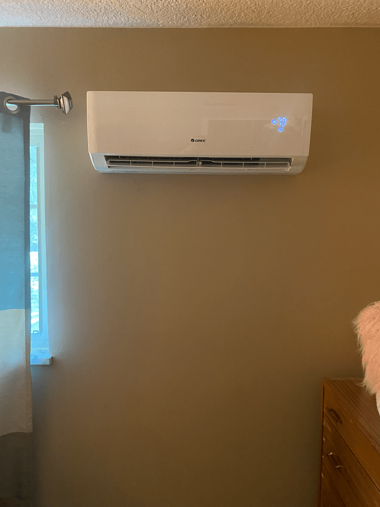 A wall-mounted air conditioning unit displaying a temperature of 75 degrees fahrenheit in a room with tan walls.